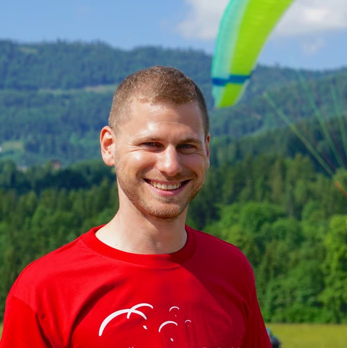 Philipp Haenggi smiling in a red shirt in front of a mountain landscape.