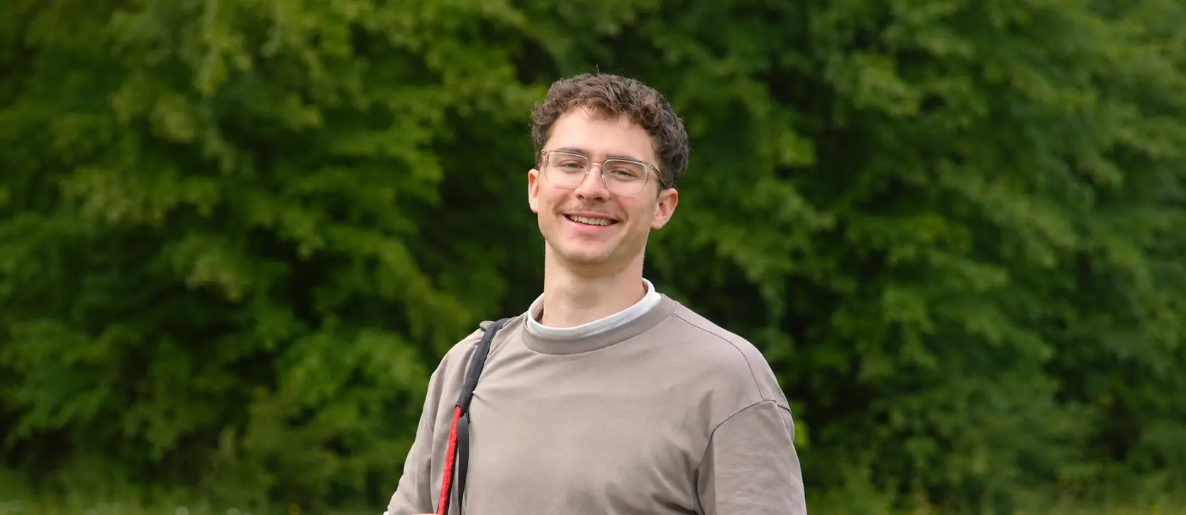 Portrait of tandem pilot Max Mayer with glasses and a mustache, smiling against a blurry green background.